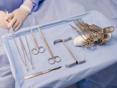 Sterile surgical instruments on a blue drape in an operating room – forceps, scissors, scalpel and clamps neatly arranged on a prep tray